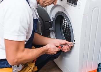 cropped view of adult repairman working with screwdriver while repairing washing machine in bathroom