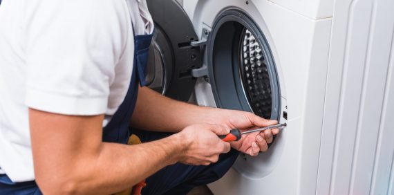 cropped view of adult repairman working with screwdriver while repairing washing machine in bathroom